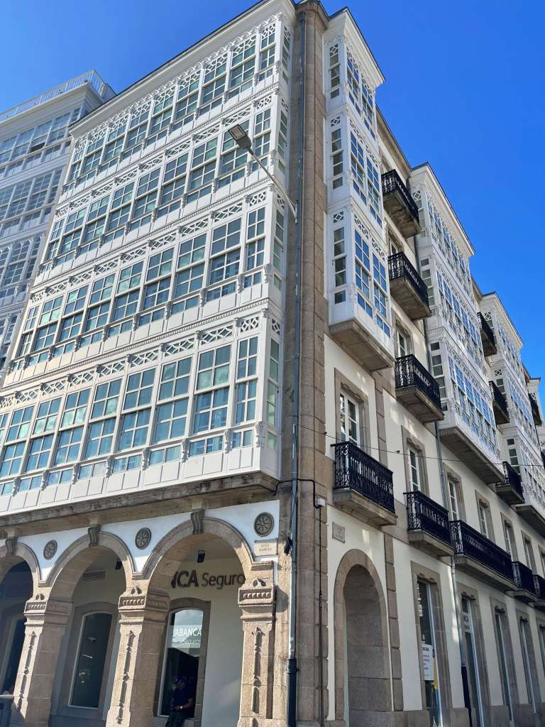 Edificio de La Marina en A Coruña en día despejado con todos los cristales de las galerías reflejando el sol 