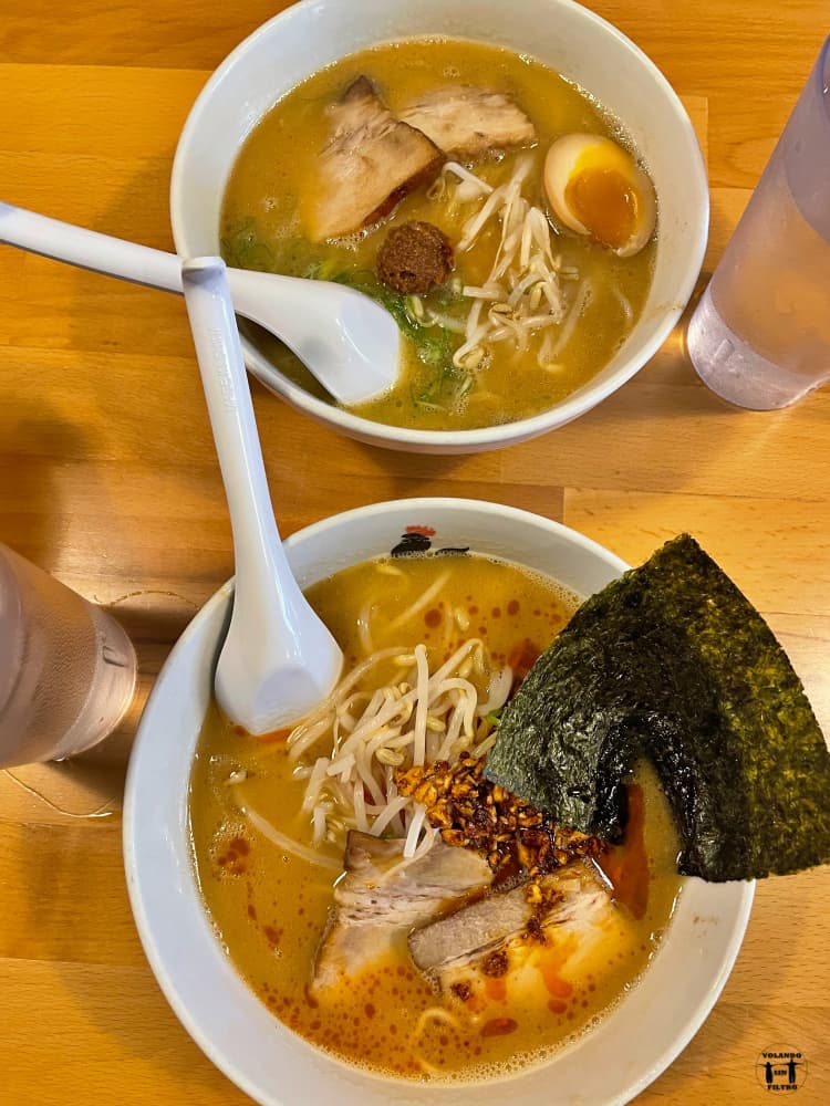 Dos boles de ramen con las cucharas dentro y dos vasos de agua a los lados