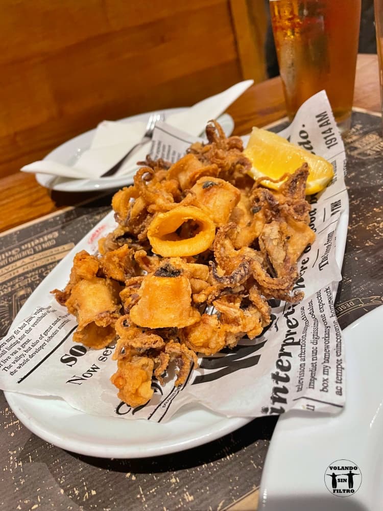 Ración de calamares en una bandeja con rodaja de limón y platos al fondo para servir