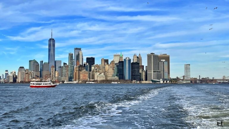 Vistas desde el ferry de Statend Island de los rascacielos de Nueva York con una pequeña barca roja en el medio y gaviotas en el horizonte 