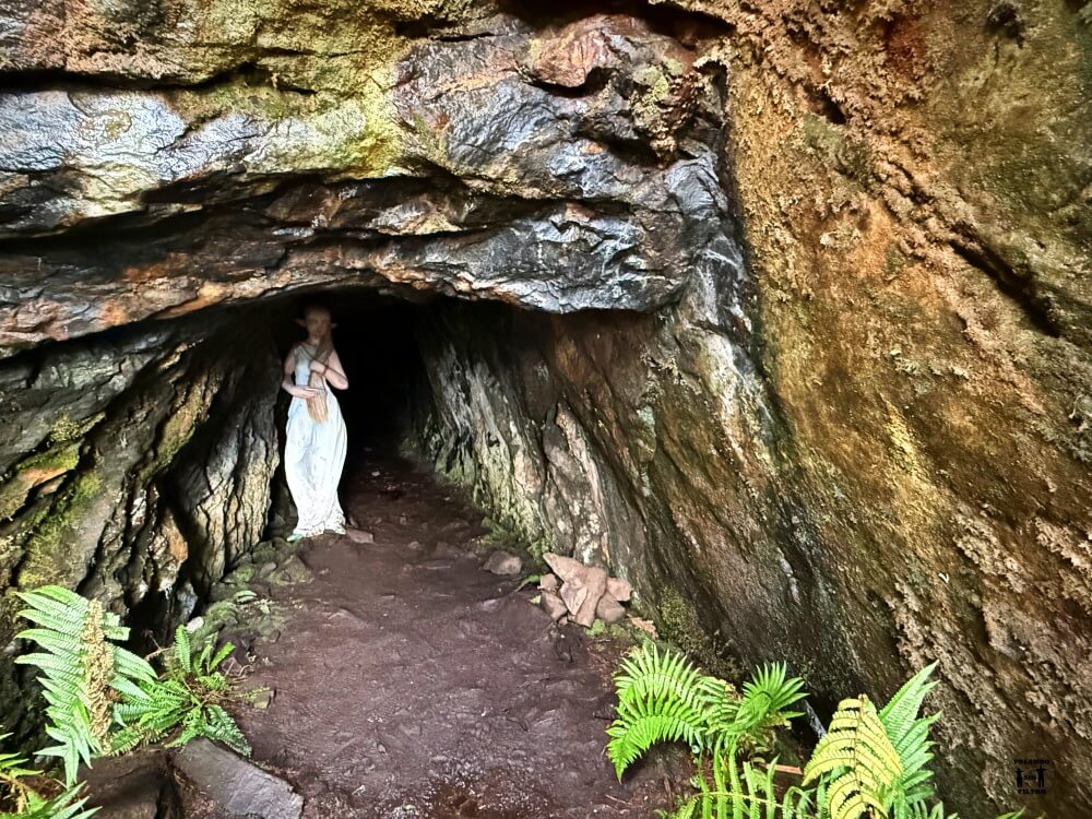 Es la entrada de una cueva que está oscura, en la imagen se puede ver la escultura de A Moura, una mujer vestida de blanco con pelo largo rubio 