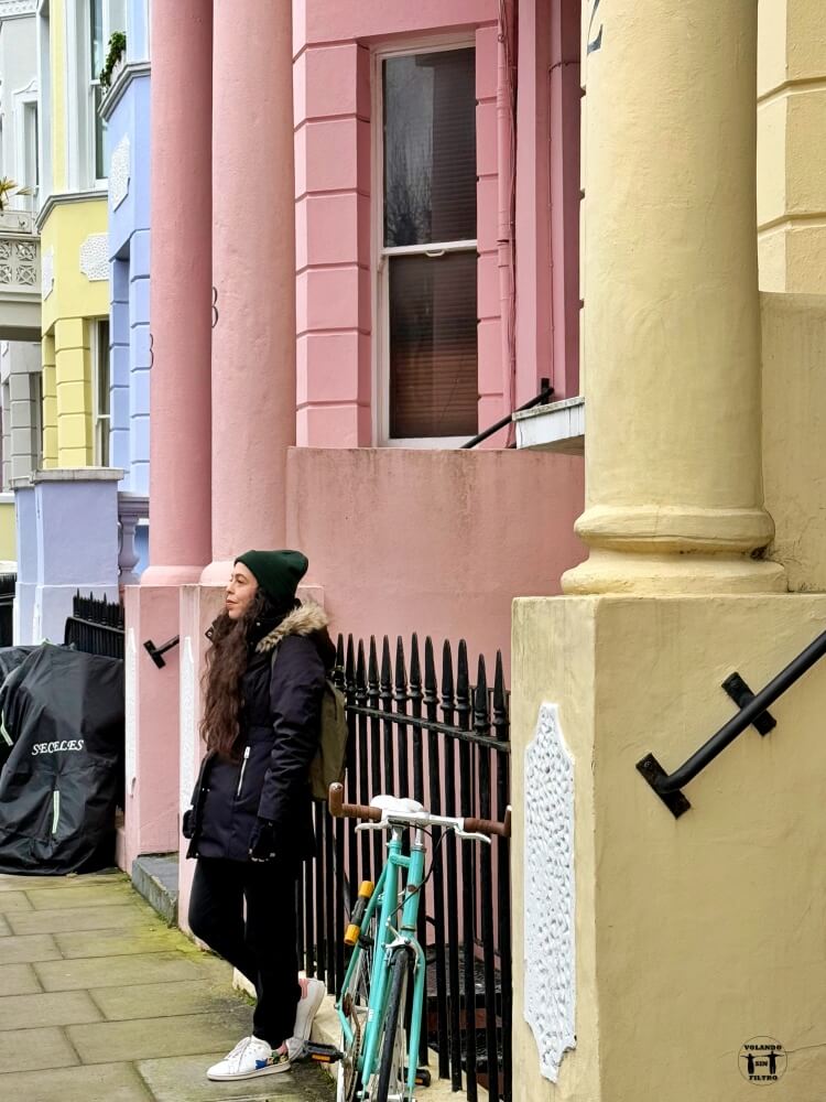 Sandra apoyada en una valla con casas de colores en la parte de atrás 