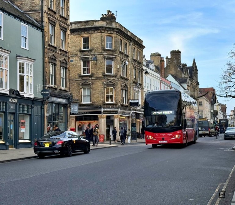 Se ve la calle principal con un autobús rojo en el medio y los edificios en segundo plano 
