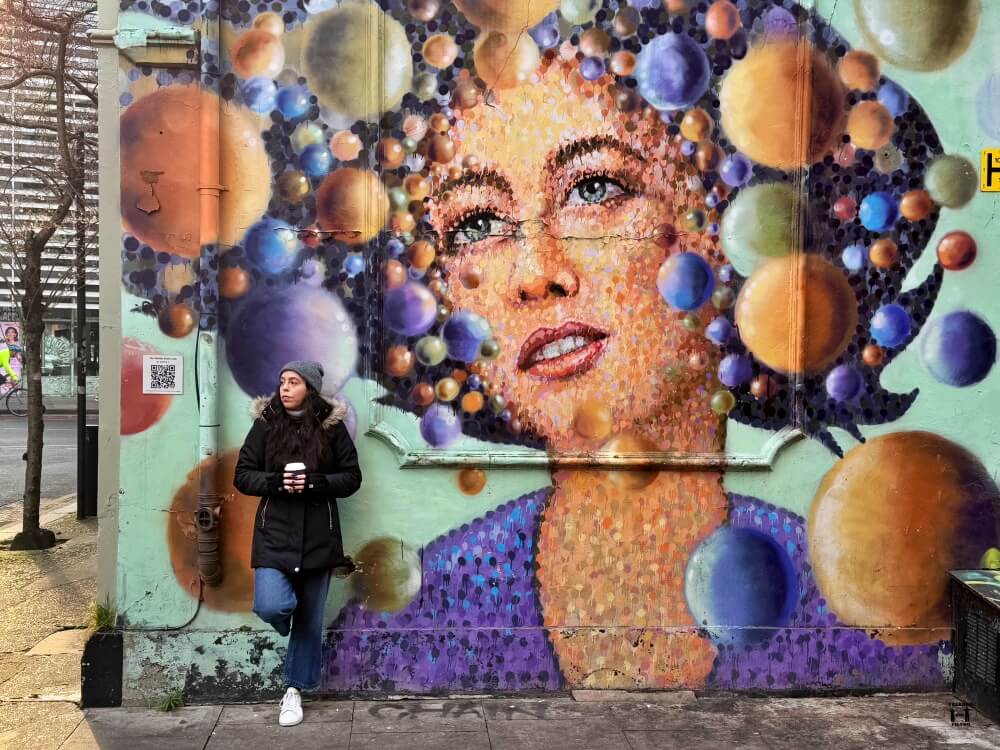 Sandra delante de una pared apoyada con un grafiti detrás de una chica con un montón de burbujas 