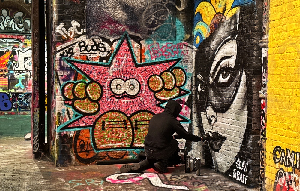 Se ve un grafiteros pintando un mural de la cara de una chica en blanco y negro 