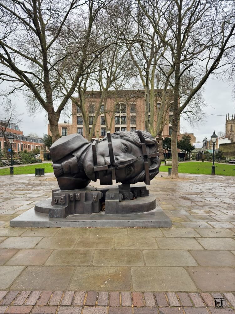 Vista general de la plaza con una escultura delante. 