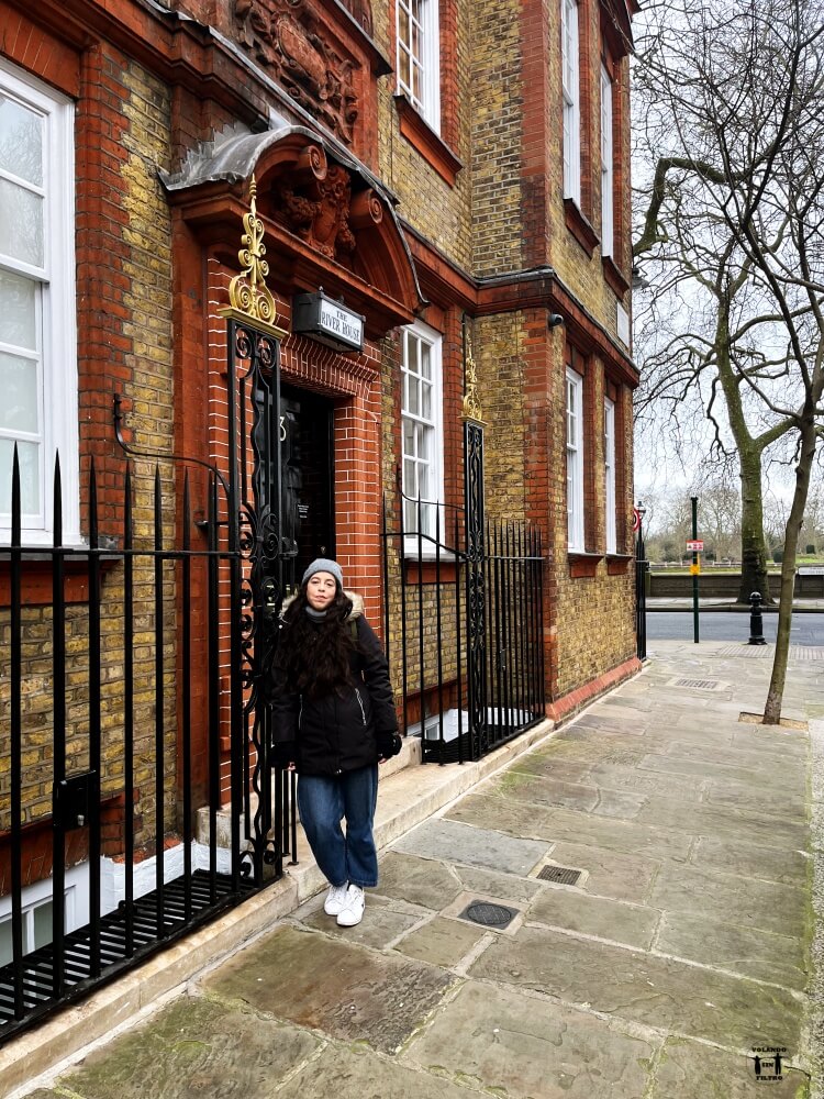 Está Sandra apoyada en una verja de un edificio de ladrillos rojos 