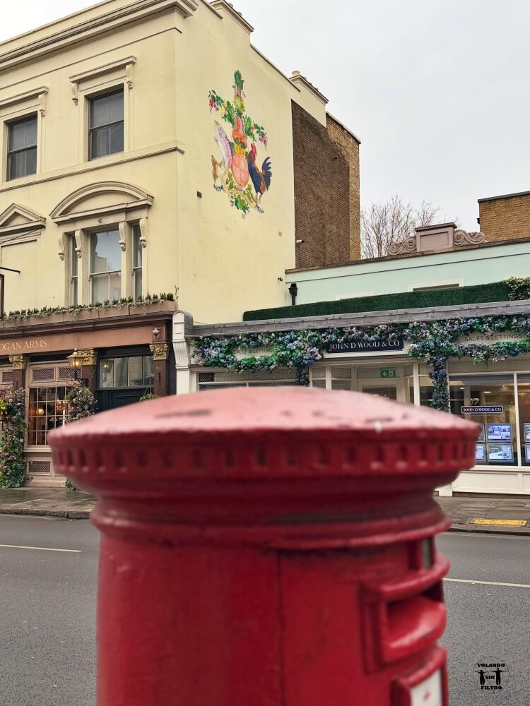En primer plano hay una boca de incendio, de fondo un edificio con un mural bonito de flores