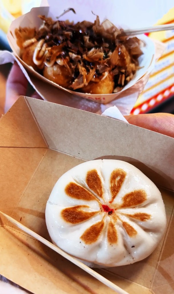 Se ve en primer plano un par de platos callejeros, en concreto un bun relleno y unos takoyaki