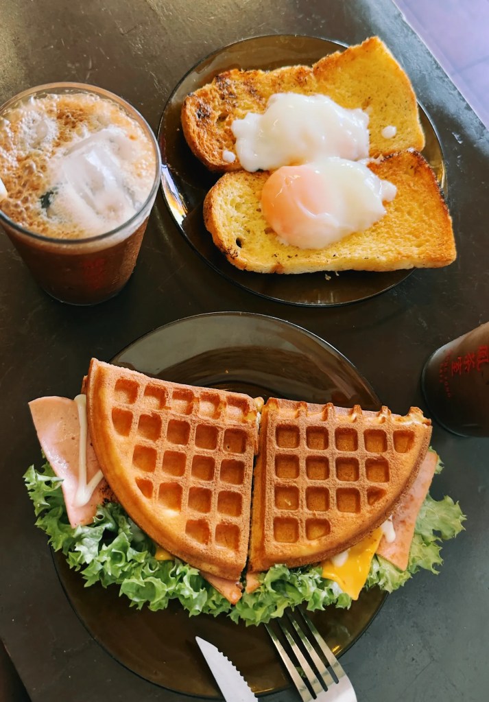 Mesa con café encima, plato de gofre y plato de tostadas con huevo